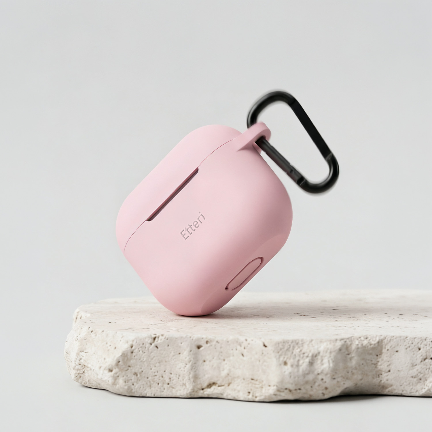 Una custodia rosa per auricolari con clip nera poggia su una pietra.