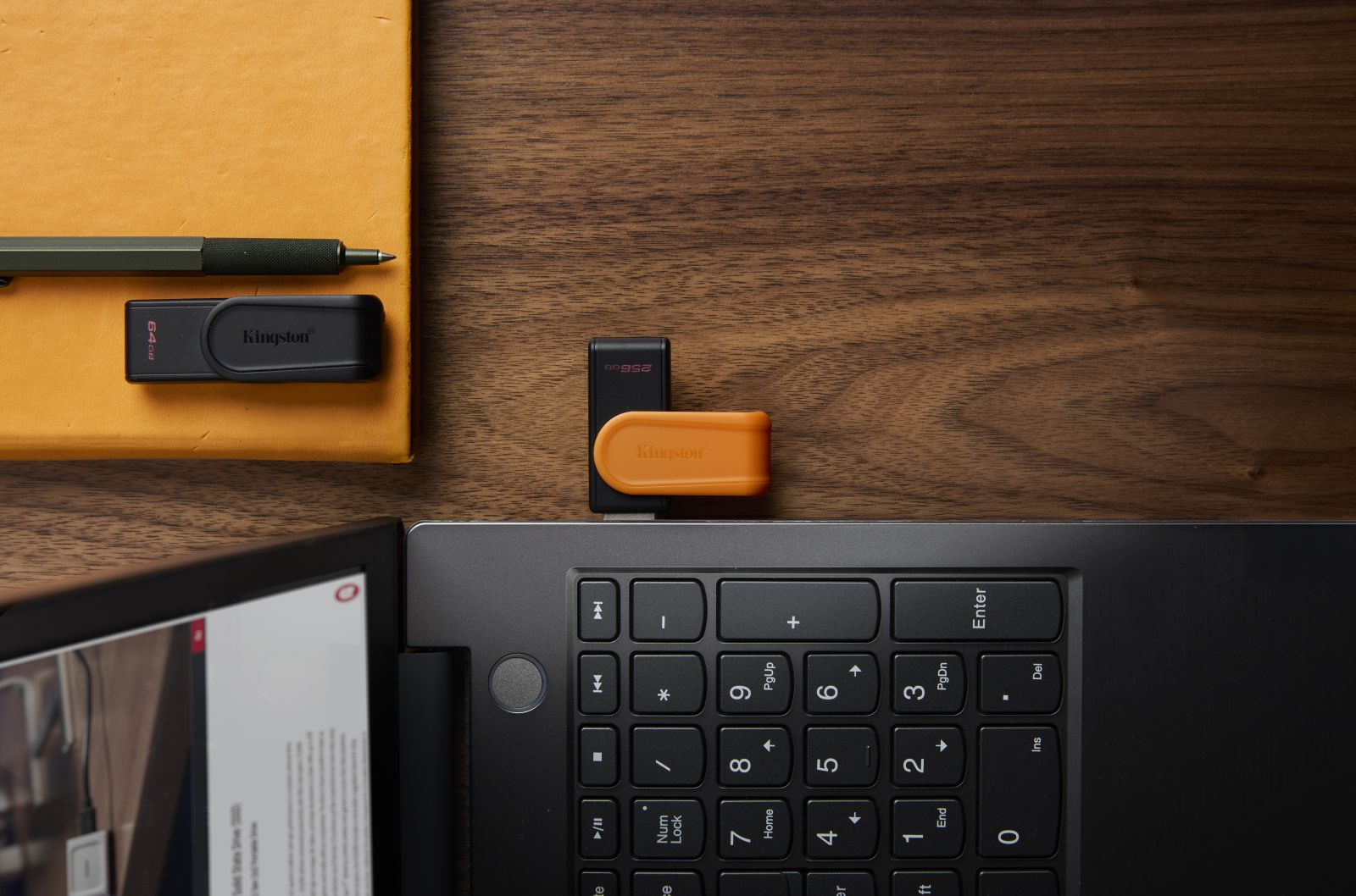 Ein schwarzer Kingston 64GB USB-Stick liegt neben einem Stift auf einem gelben Notizblock.