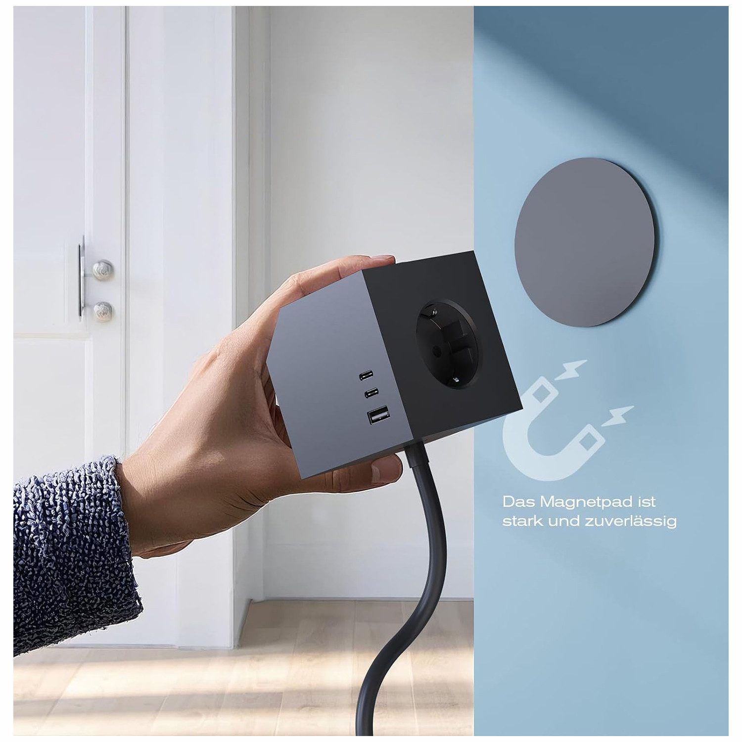 Hand hält eine graue Steckdosenleiste mit USB-Anschlüssen vor einer blauen Wand mit Magnet-Symbol.