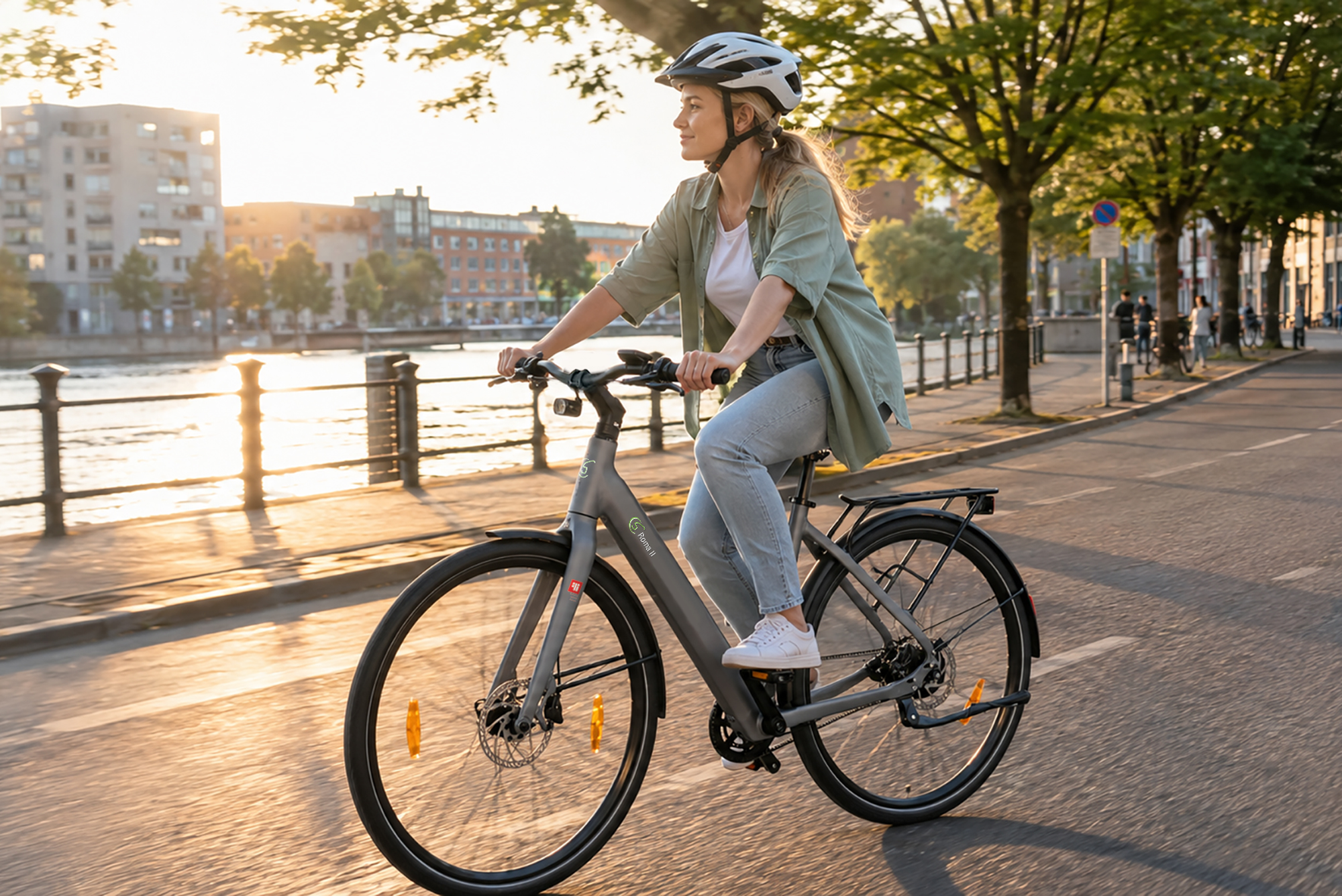 Eine Frau mit Helm fährt Rad am Wasser entlang, Gebäude im Hintergrund.