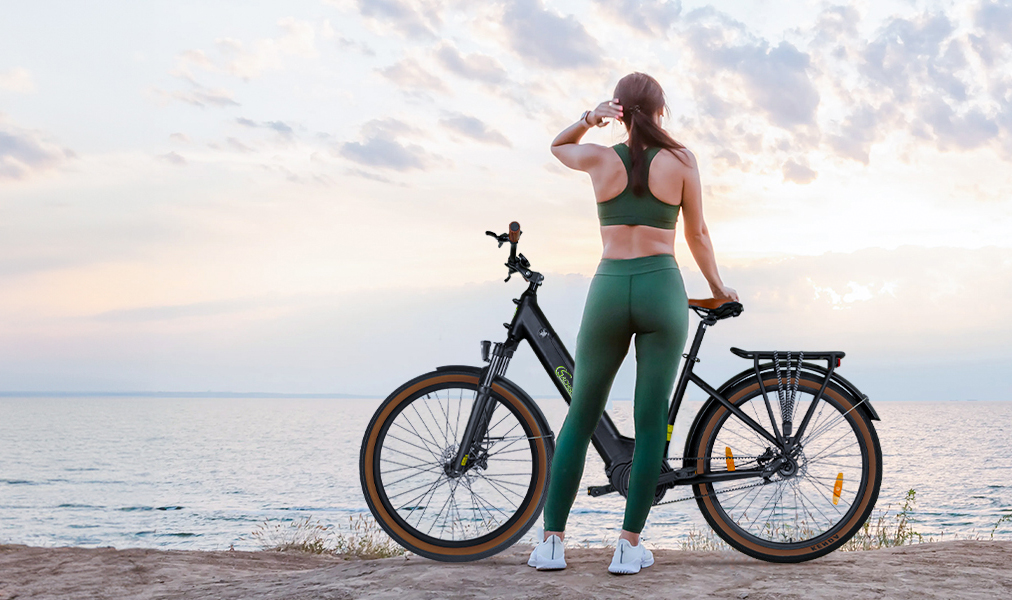 Frau in Sportkleidung am Meer neben einem Fahrrad bei Sonnenuntergang.