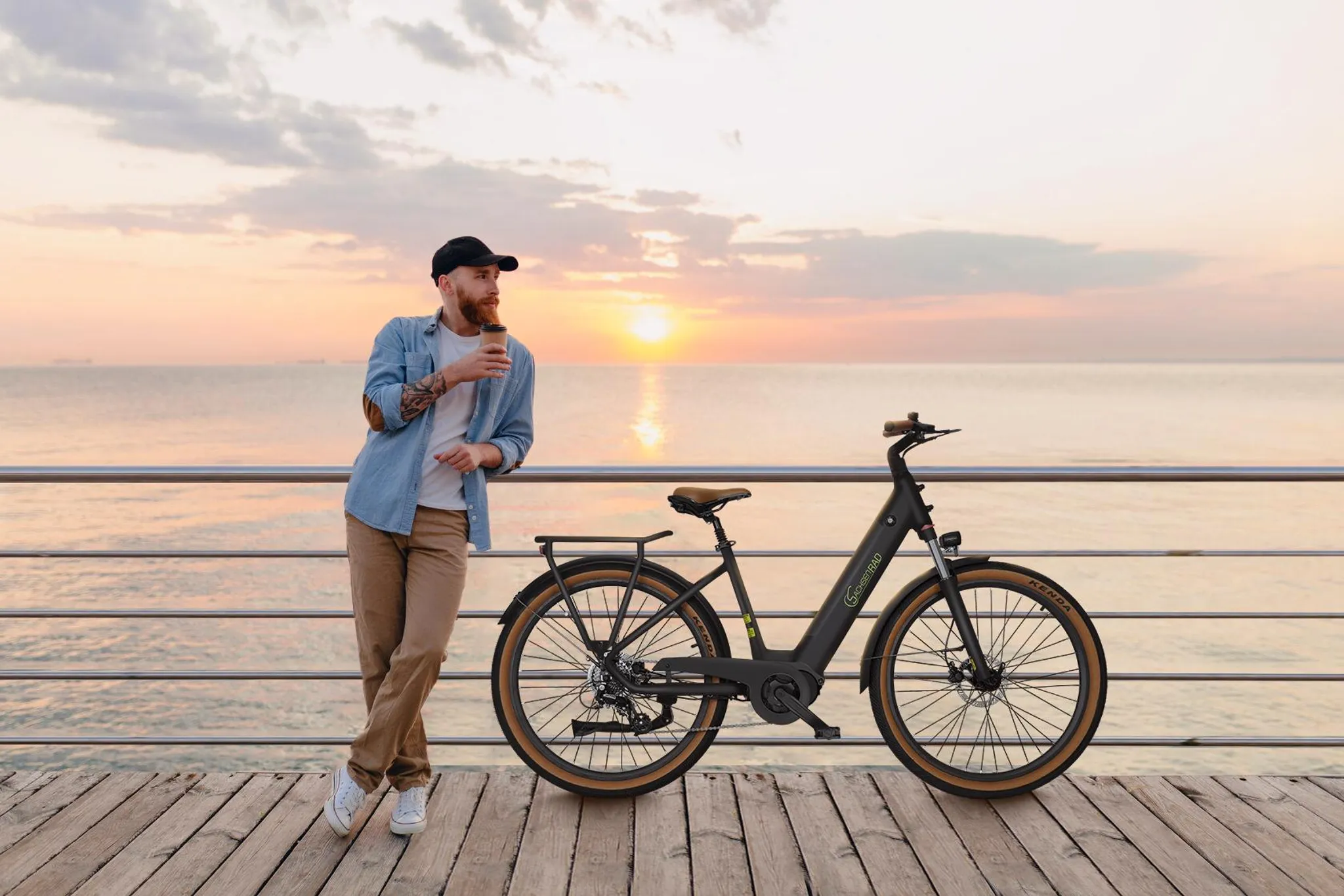Mann mit Kaffee und Fahrrad am Meer bei Sonnenuntergang.