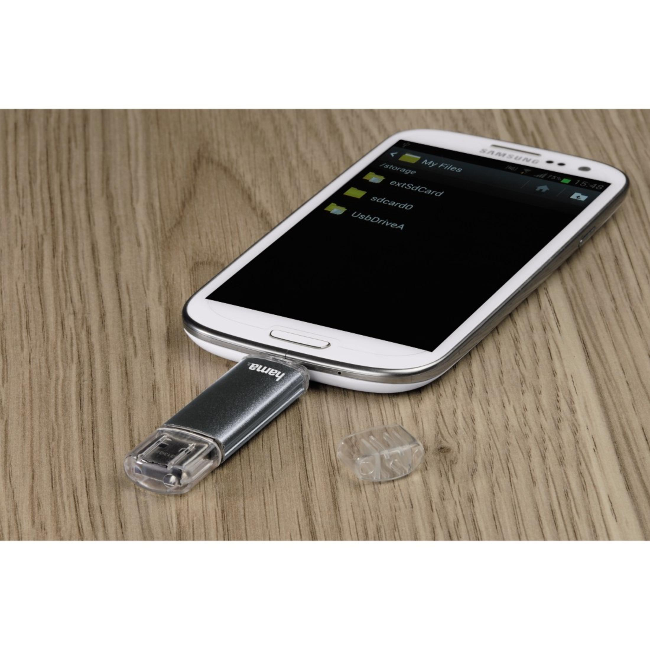 Ein USB-Stick mit Hama-Logo ist in ein Smartphone auf einem Holztisch eingesteckt.
