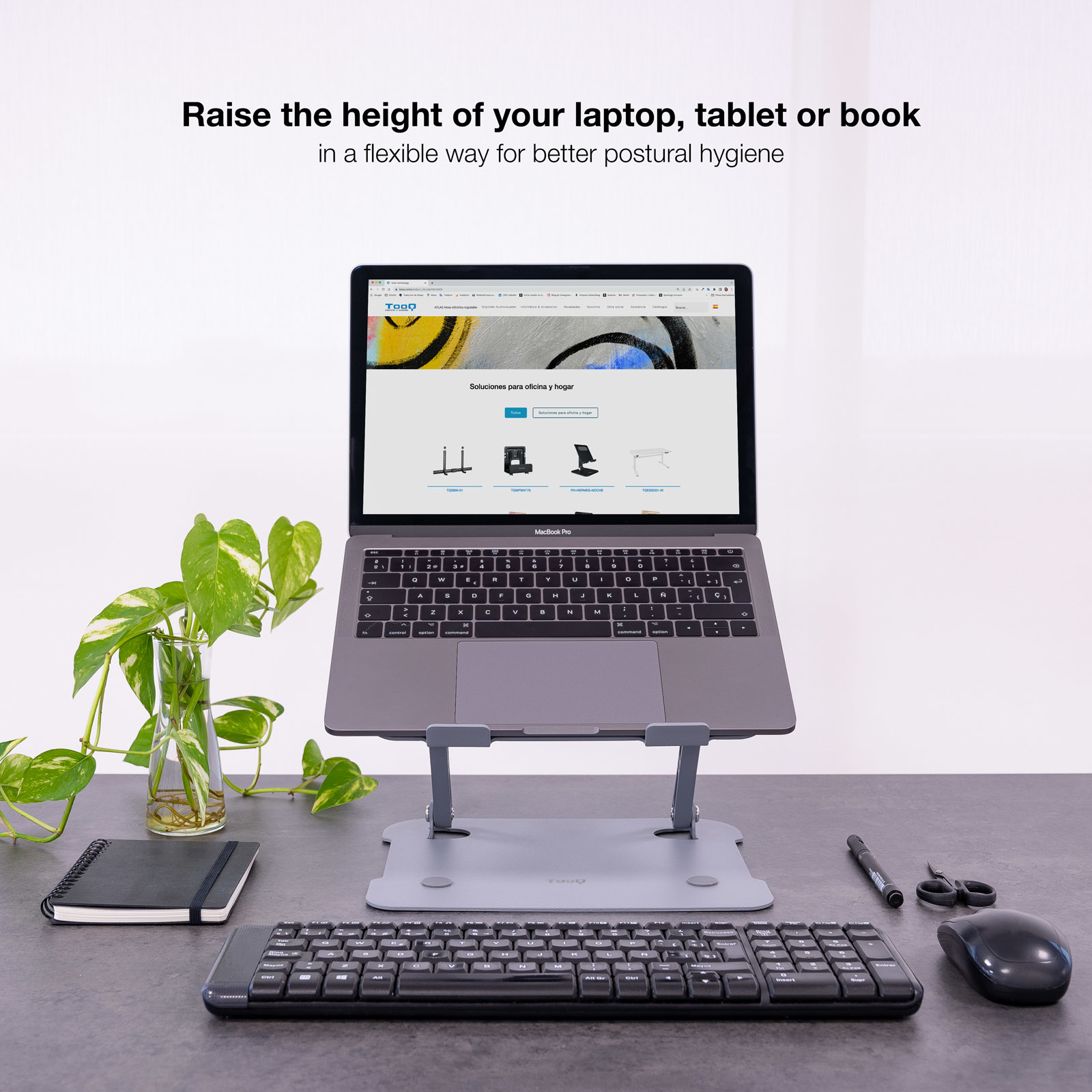 Ein Laptop auf einem silbernen Ständer mit Tastatur, Maus, Schere, Stift und Pflanze.