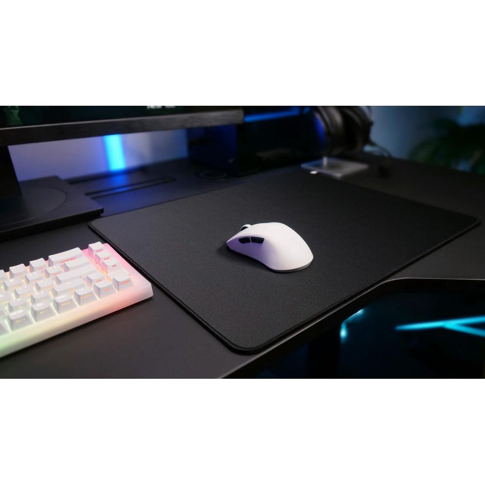 Eine weiße Maus liegt auf einem schwarzen Mauspad neben einer Tastatur.