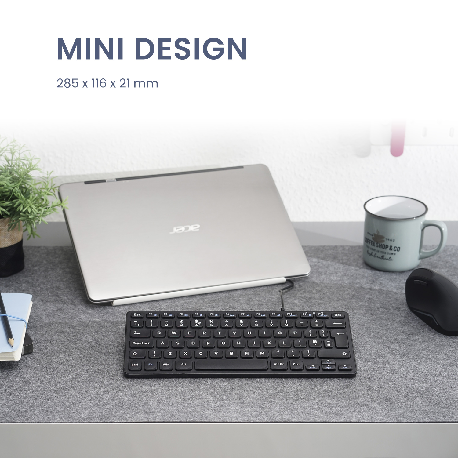 Eine kompakte schwarze Tastatur, ein Laptop, eine Maus und eine Tasse auf einem grauen Schreibtisch.