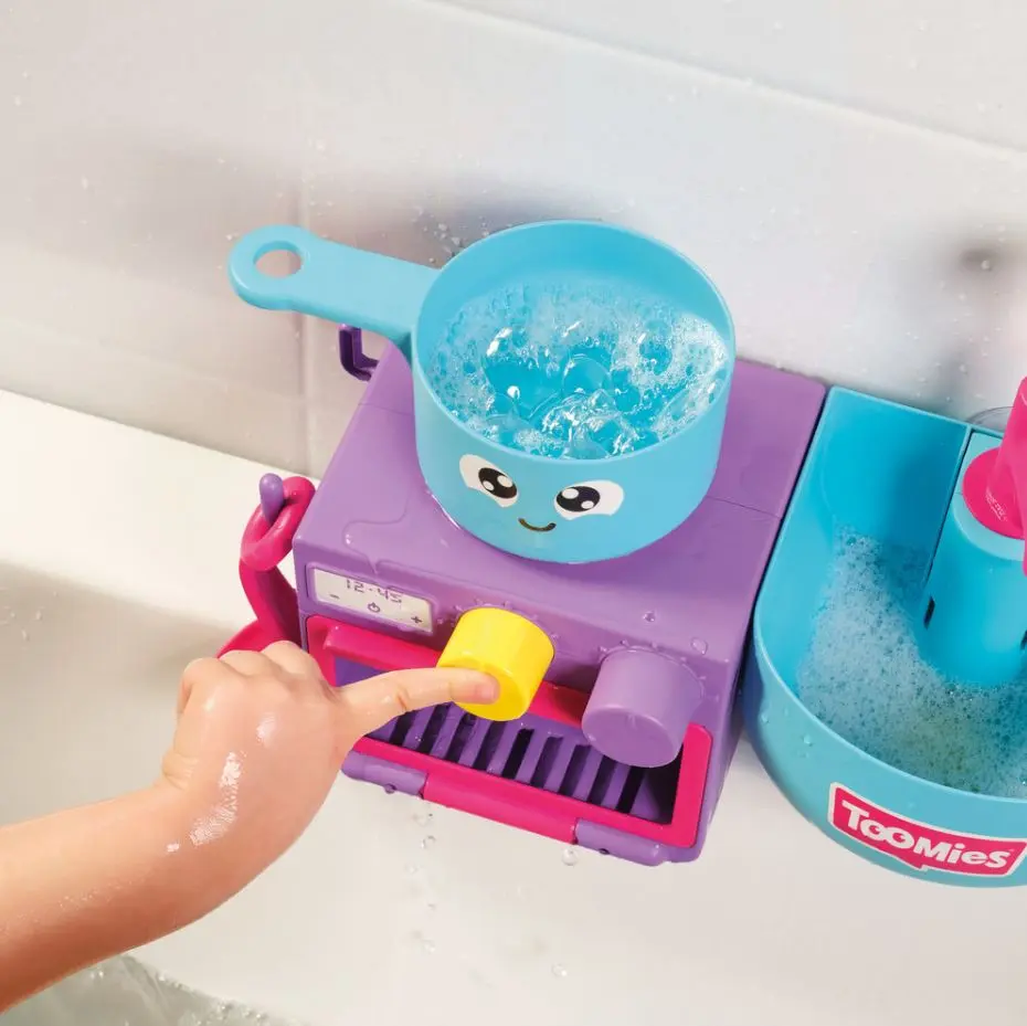 Un niño presiona un botón amarillo en un juguete colorido en la bañera.