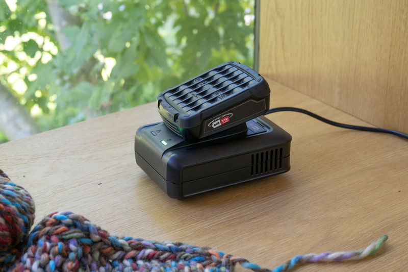 Un caricabatterie nero con una batteria sopra è appoggiato su una superficie di legno.