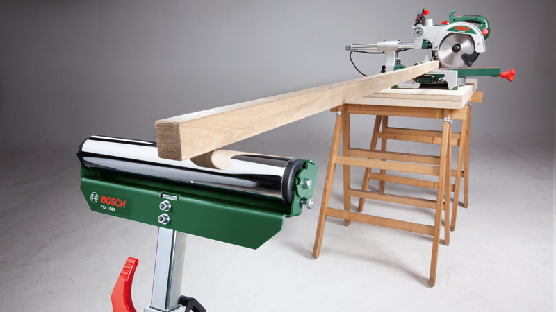 Ein Gehrungssäge mit Holz auf einem Tischbock und einer grünen Bosch-Rolle.