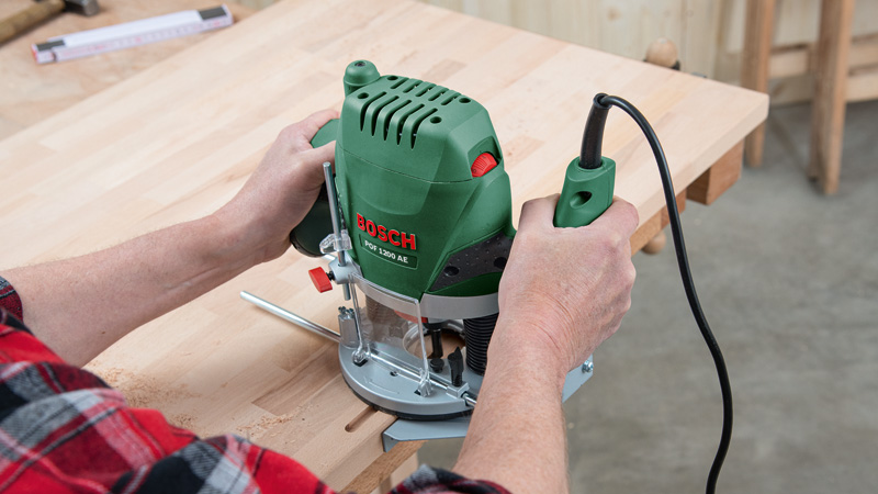 Persona che usa un utensile Bosch verde su un tavolo di legno con segatura.