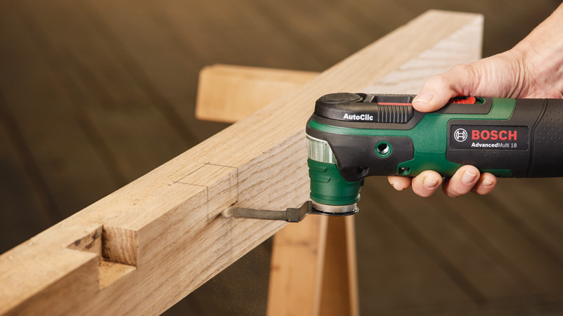 Mano sujetando herramienta oscilante Bosch cortando madera. Se levanta polvo.