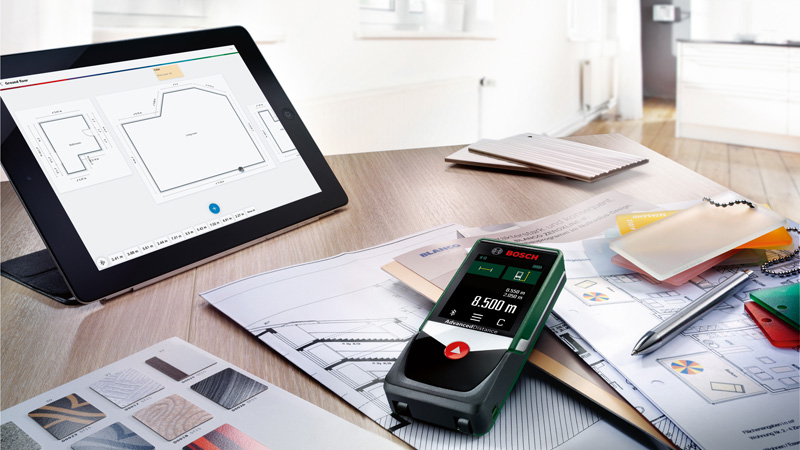 Une tablette avec des plans d'étage, un télémètre Bosch et des plans sur une table en bois.