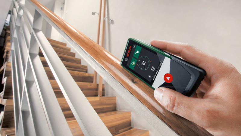 Une main tient un appareil de mesure Bosch vert mesurant un escalier.