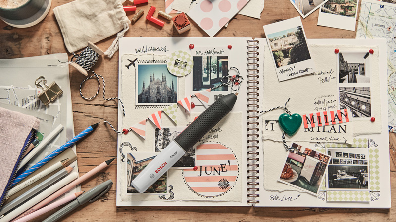 Un álbum abierto con fotos, bolígrafos y decoraciones de viaje sobre una mesa de madera.