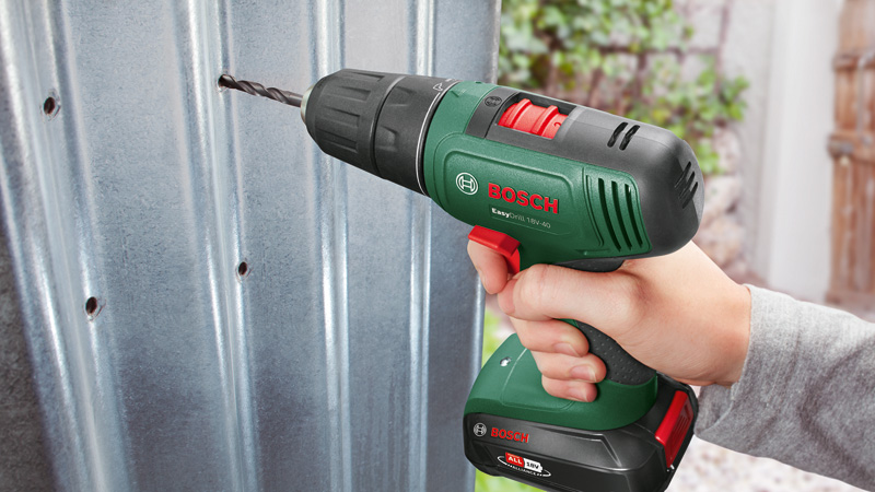 Un taladro Bosch verde con portabrocas negro perfora un agujero en metal corrugado.