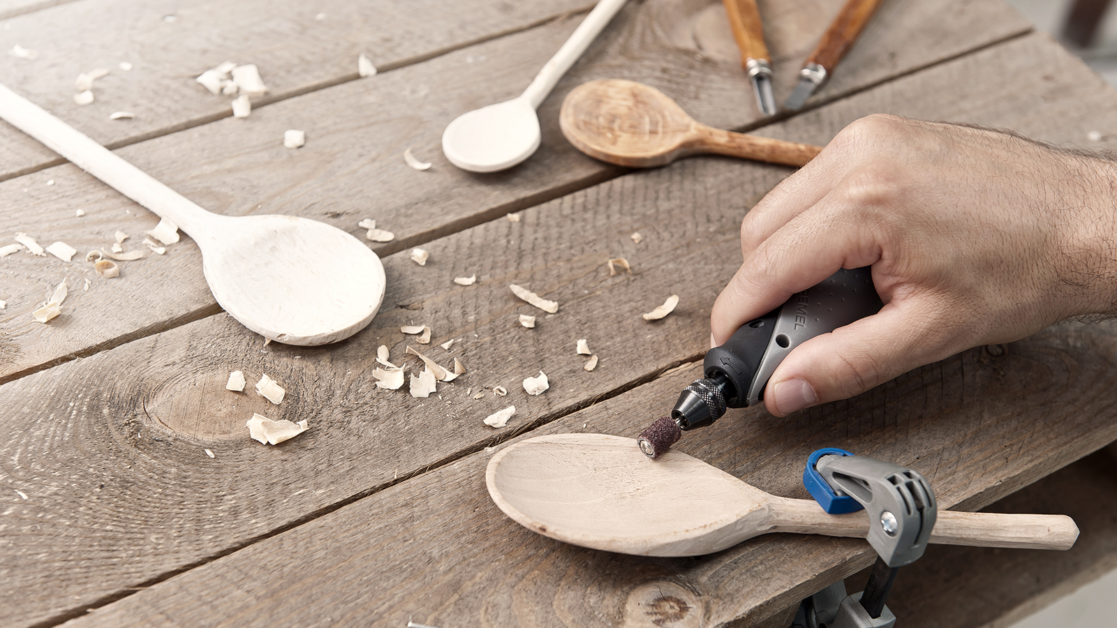 Holzlöffelherstellung mit einem Dremel-Werkzeug auf einem Holztisch.