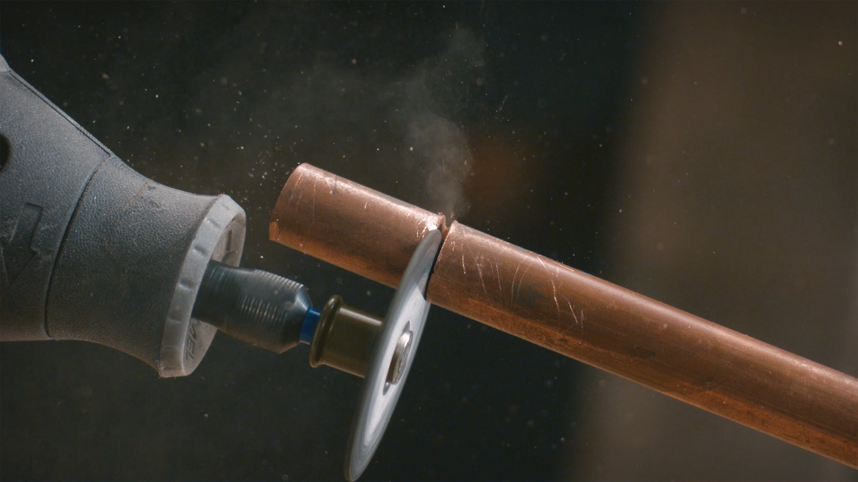 Ein Dremel schneidet ein Kupferrohr. Rauch und Partikel steigen auf.
