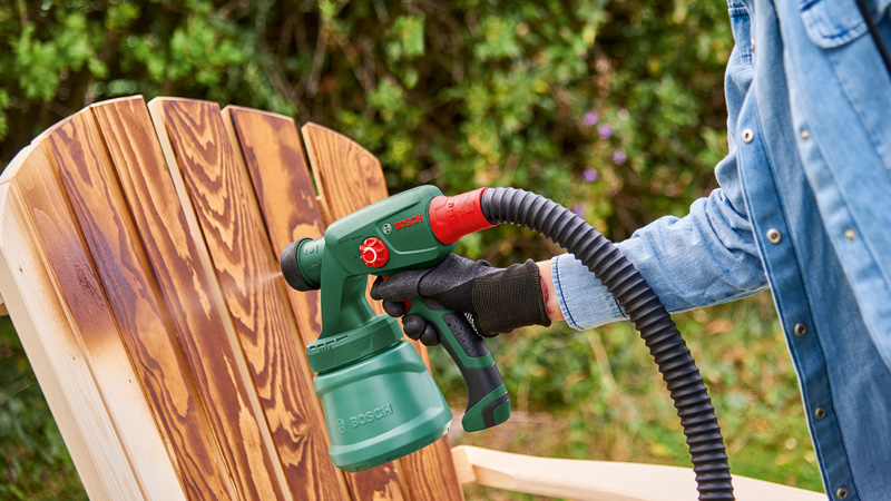 Una persona spruzza legno con una pistola a spruzzo Bosch verde all'aperto.