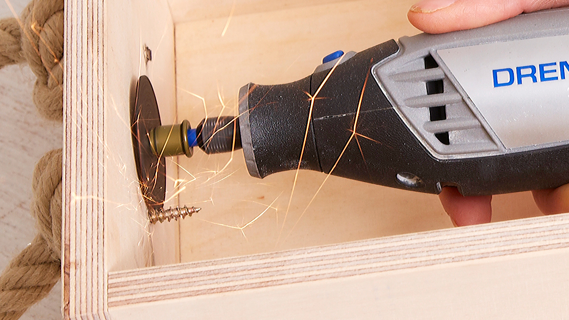 Ein Dremel-Werkzeug schneidet eine Schraube in Holz, Funken fliegen.