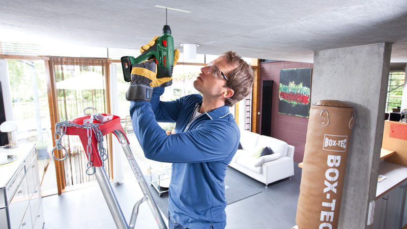 Uomo fora soffitto con trapano a batteria, in piedi su scala.