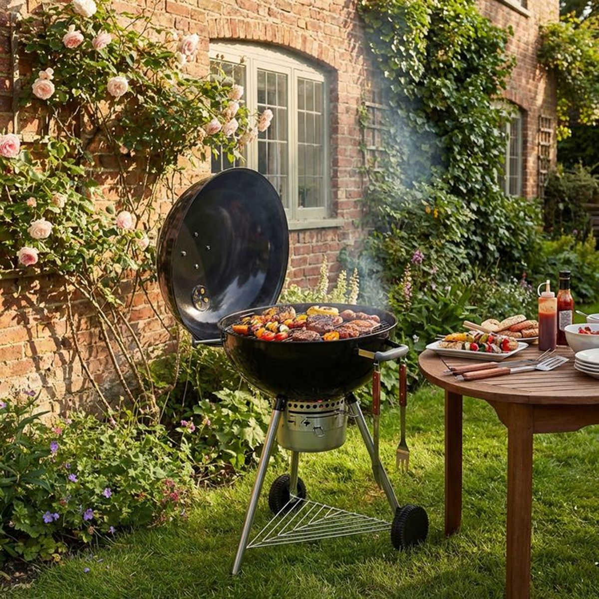 Ein Grill mit kochendem Essen, neben einem Tisch mit Tellern und Soßen.
