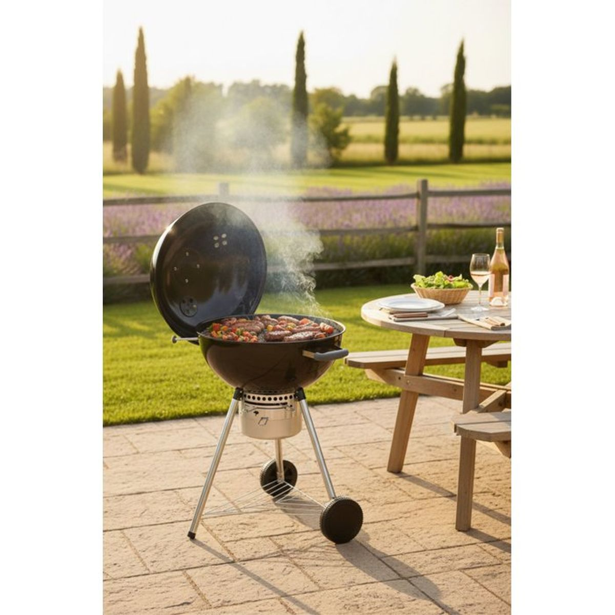 Ein runder Grill mit offenem Deckel, auf dem Würstchen und Gemüse gegrillt werden. Rauch steigt auf.