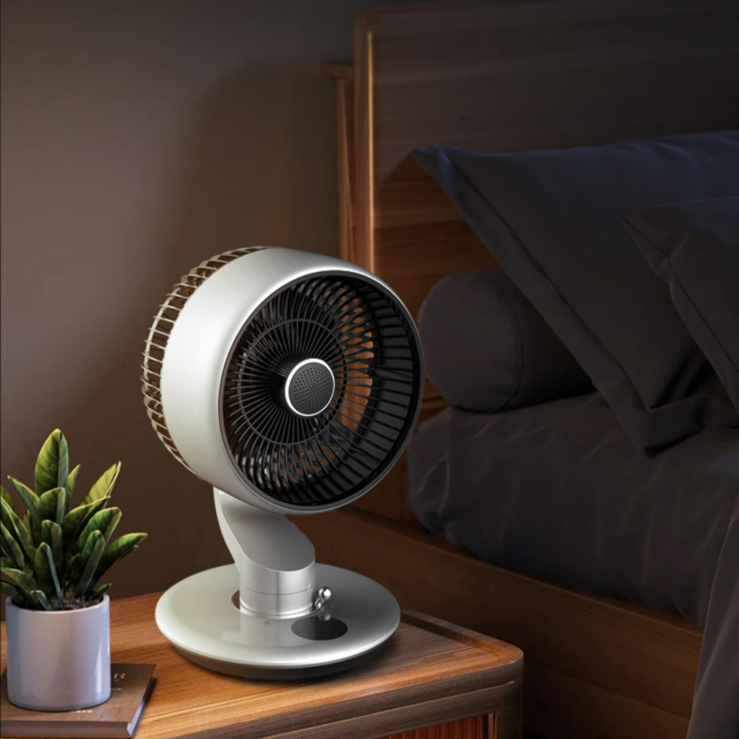 Ein silberner Ventilator steht auf einem Nachttisch neben einem Bett.