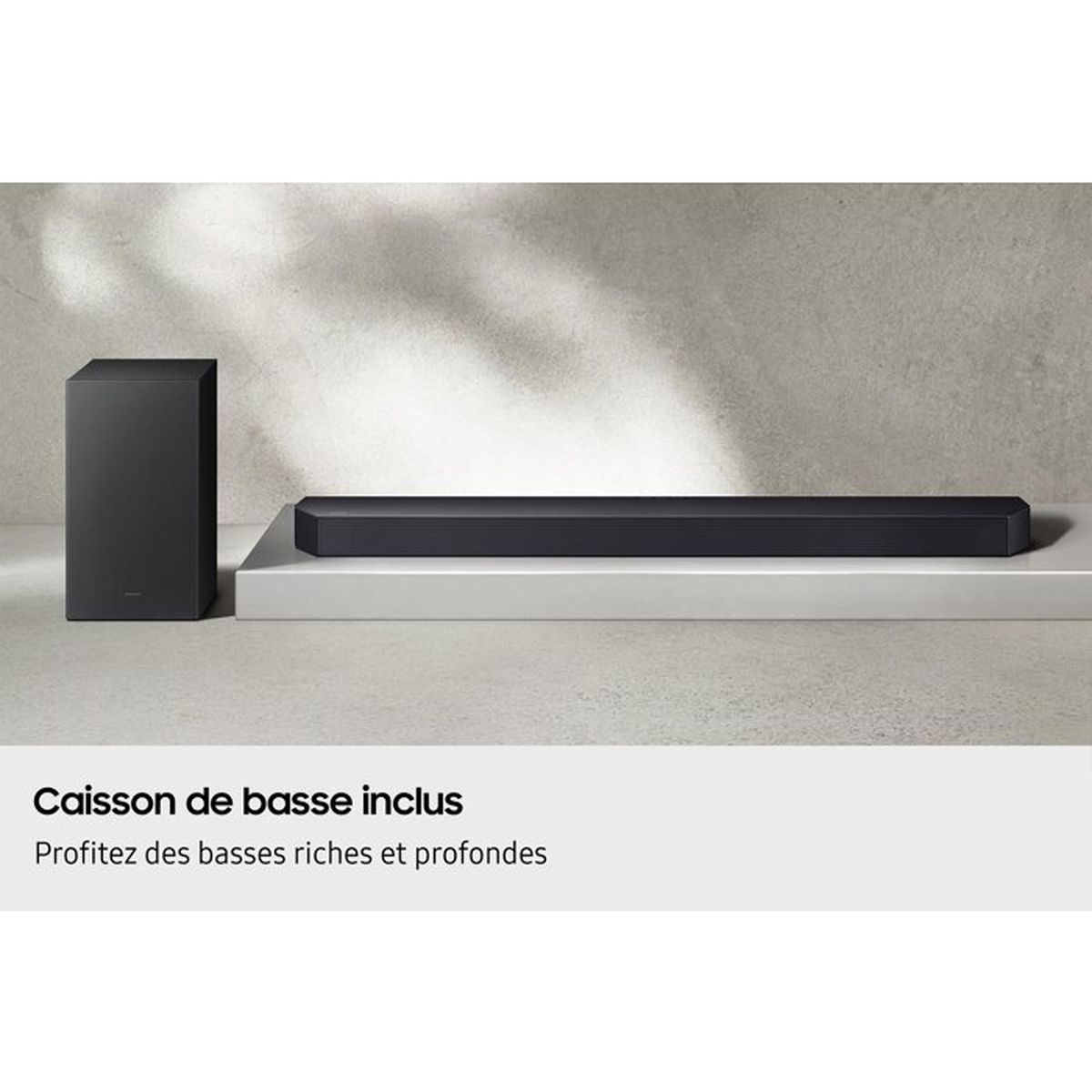 Schwarze Soundbar und Subwoofer auf einem weißen Podest vor einer grauen Wand.