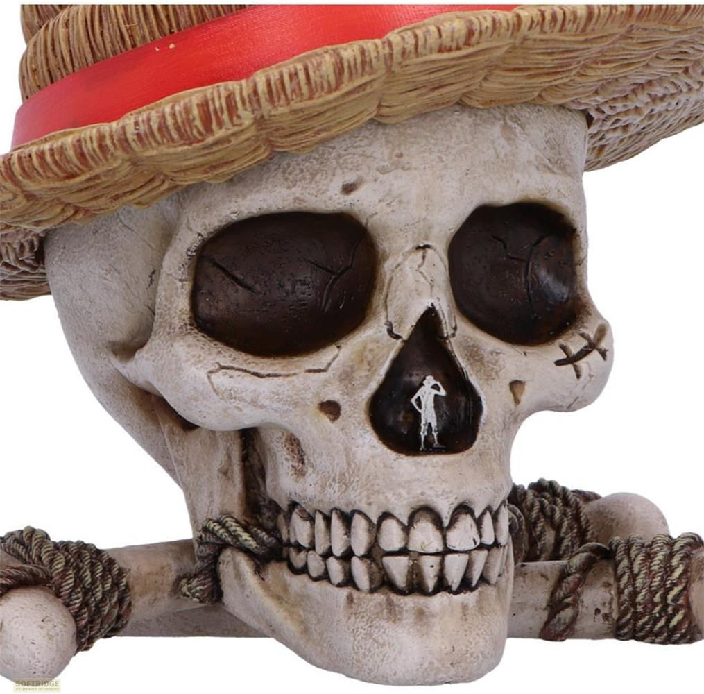 Una figura de calavera con sombrero de paja y banda roja, sostiene huesos cruzados.