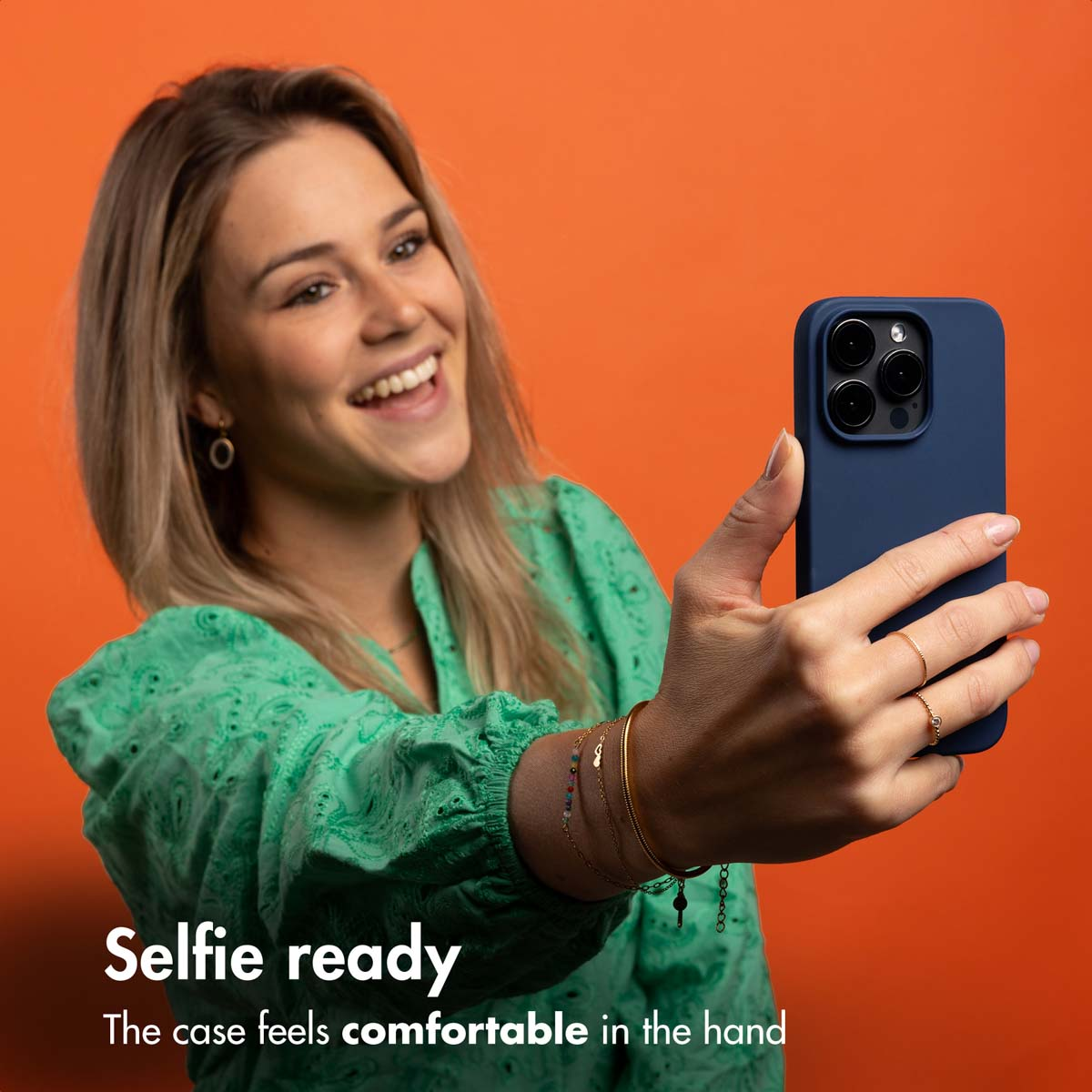 Donna scatta un selfie con custodia blu per telefono su sfondo arancione.