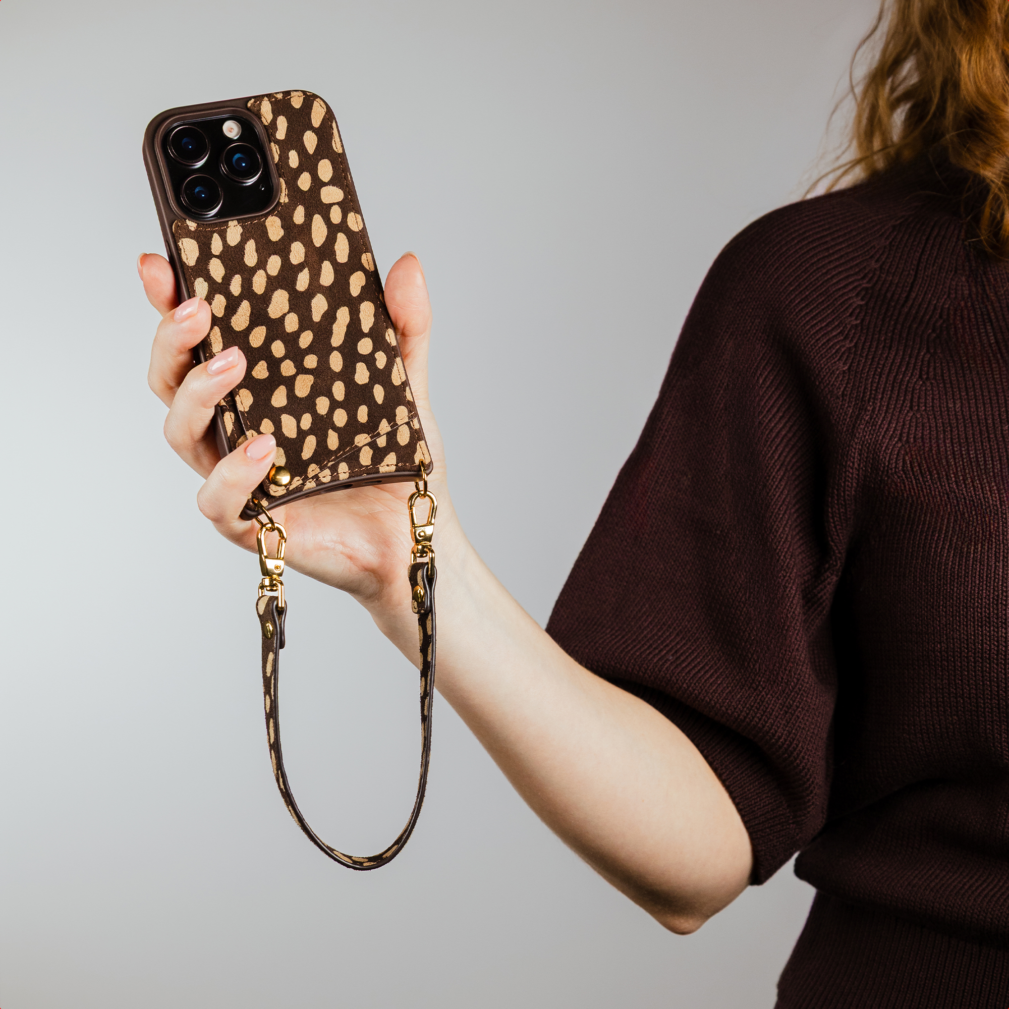 A hand holds a brown leopard print phone with a wrist strap attached.