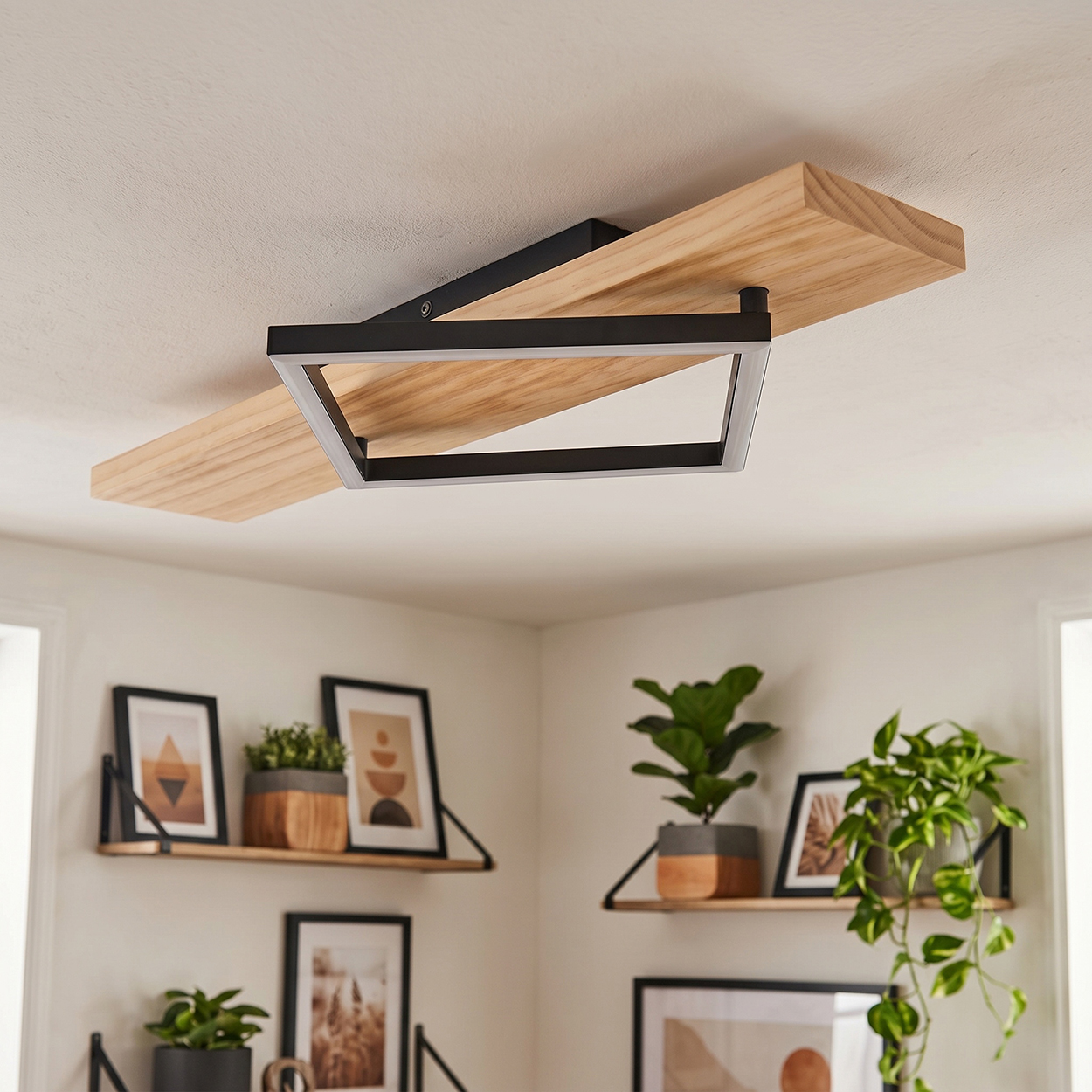 Moderne Deckenleuchte mit Holz- und schwarzem Metallrahmen über Regalen mit Pflanzen und Kunst.