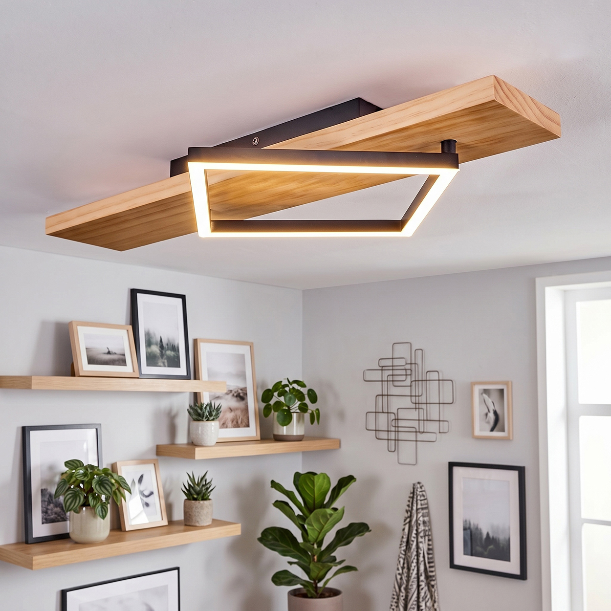 Moderne Deckenleuchte mit Holz und geometrischem Rahmen über einer Wand mit Regalen und Pflanzen.