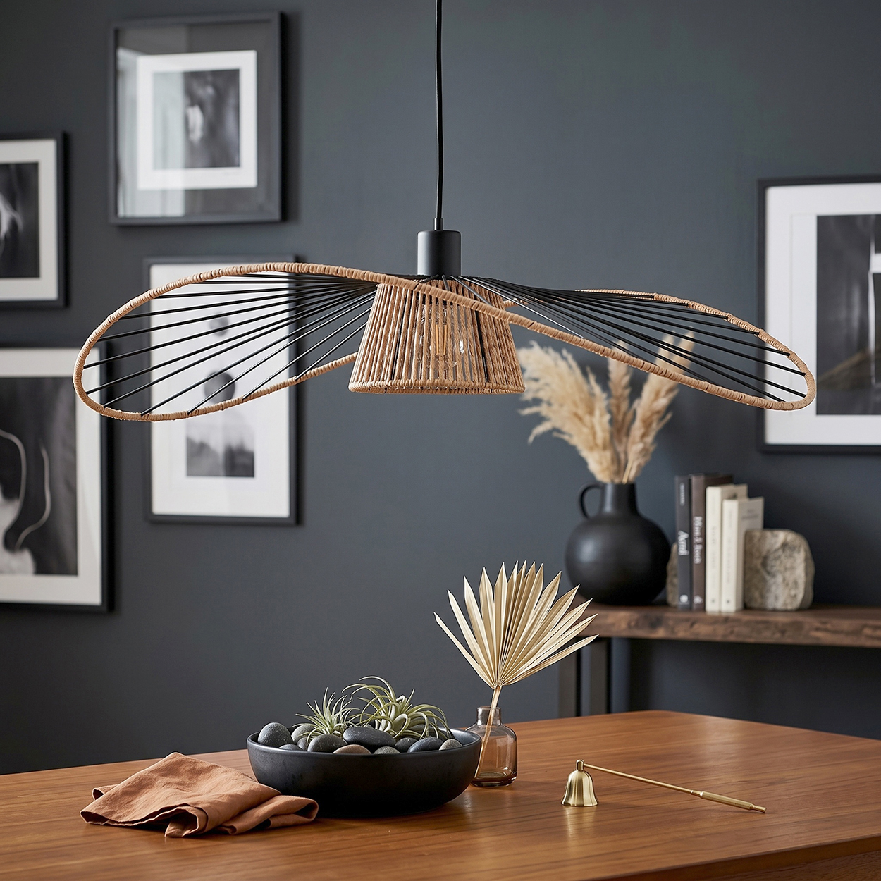 Ein moderner Lampenschirm aus Rattan und schwarzen Metallstreben über einem Holztisch mit Dekoration.