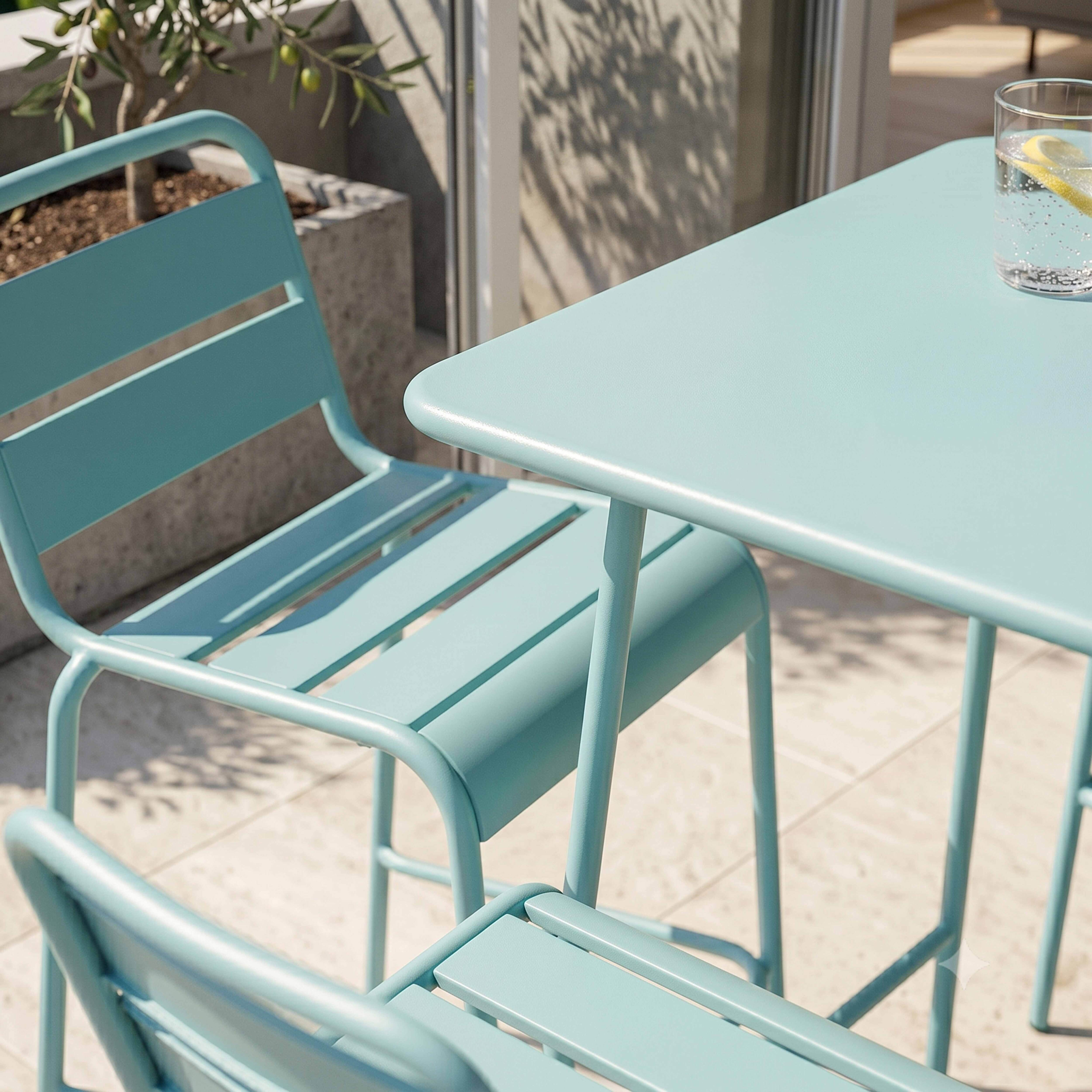 Ein türkisfarbener Metalltisch und Stühle auf einer Terrasse mit einem Glas Wasser.
