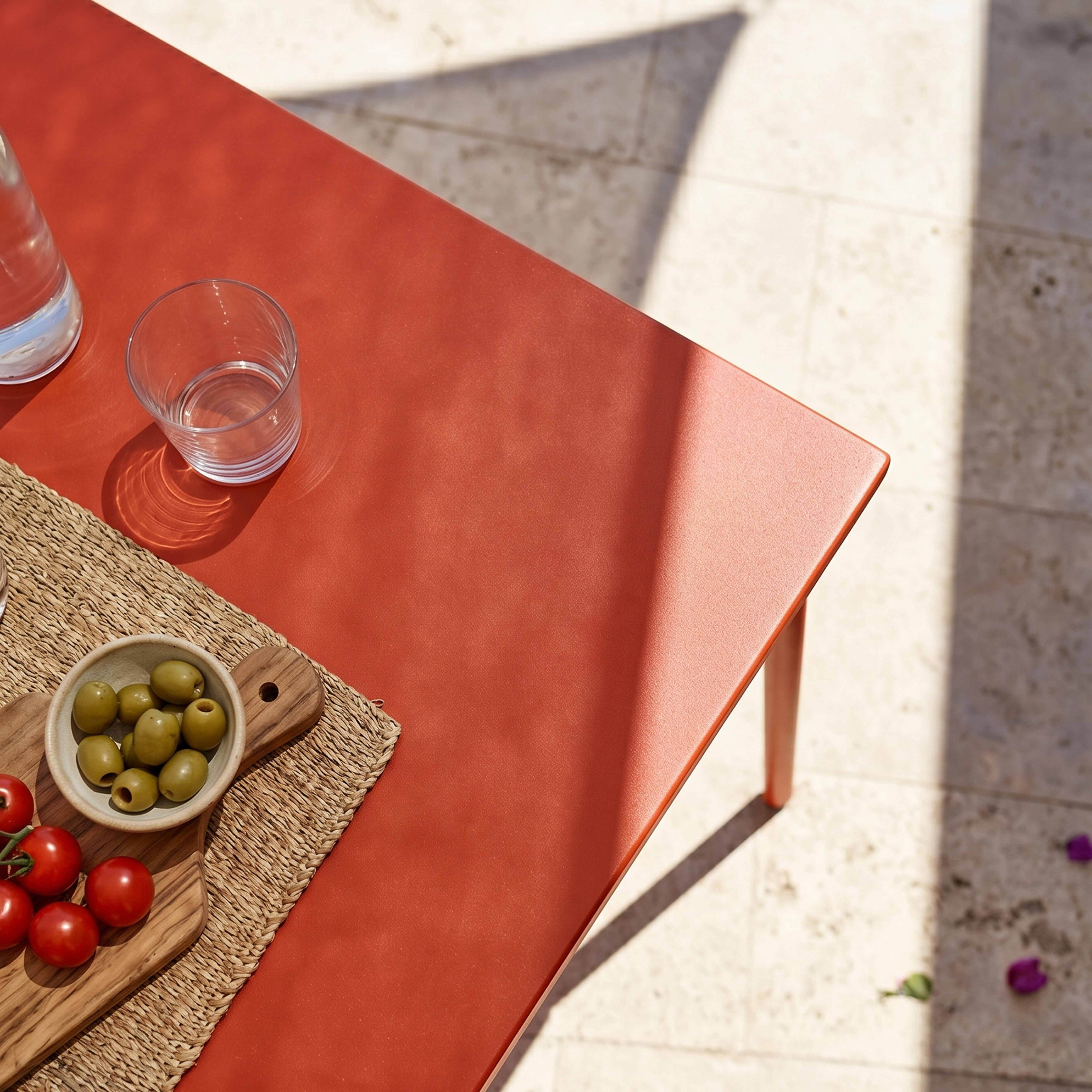 Rote Tischplatte mit Oliven, Tomaten, Wasserglas und Karaffe.
