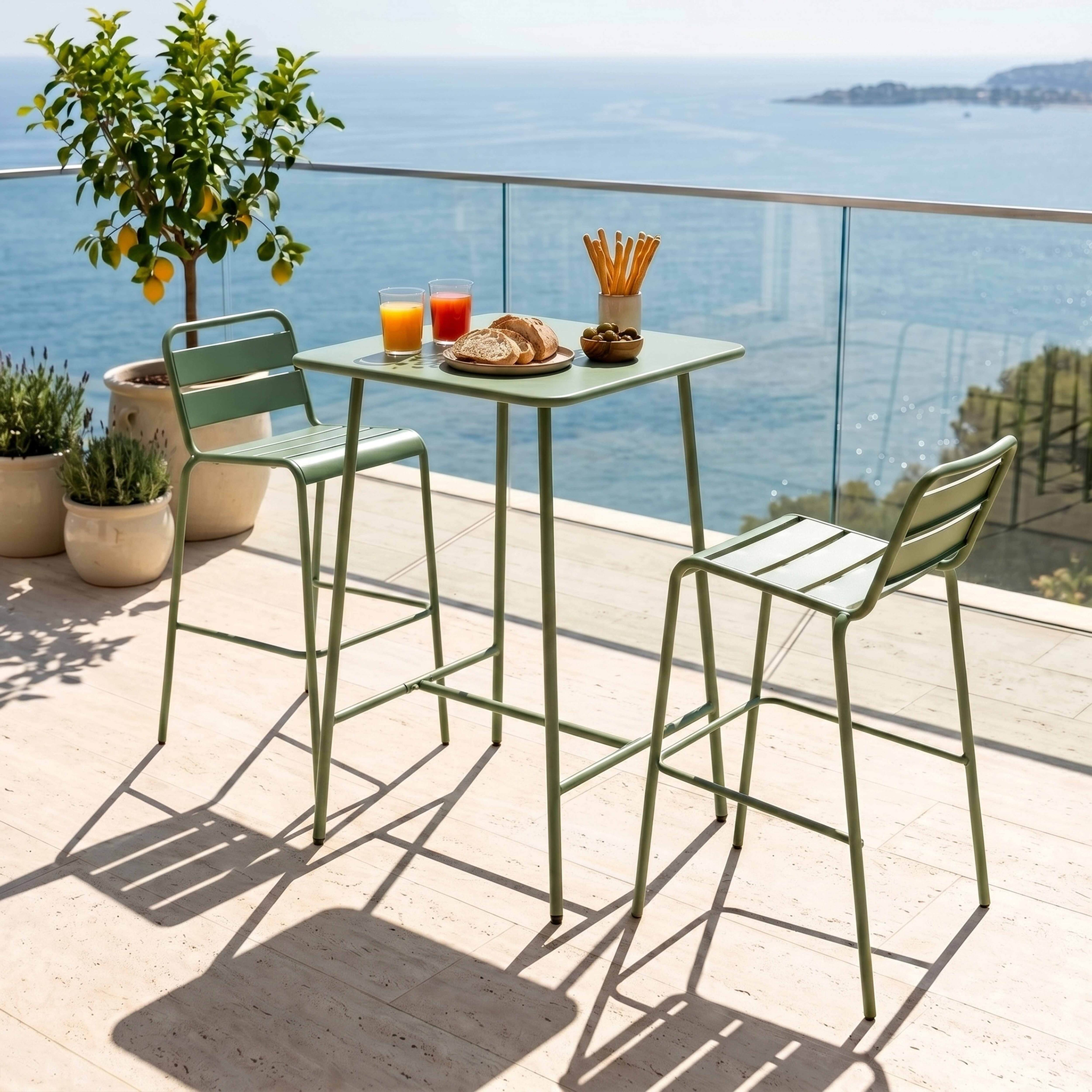 Grüne Barhocker an einem Tisch mit Getränken und Brot auf einer Terrasse am Meer.