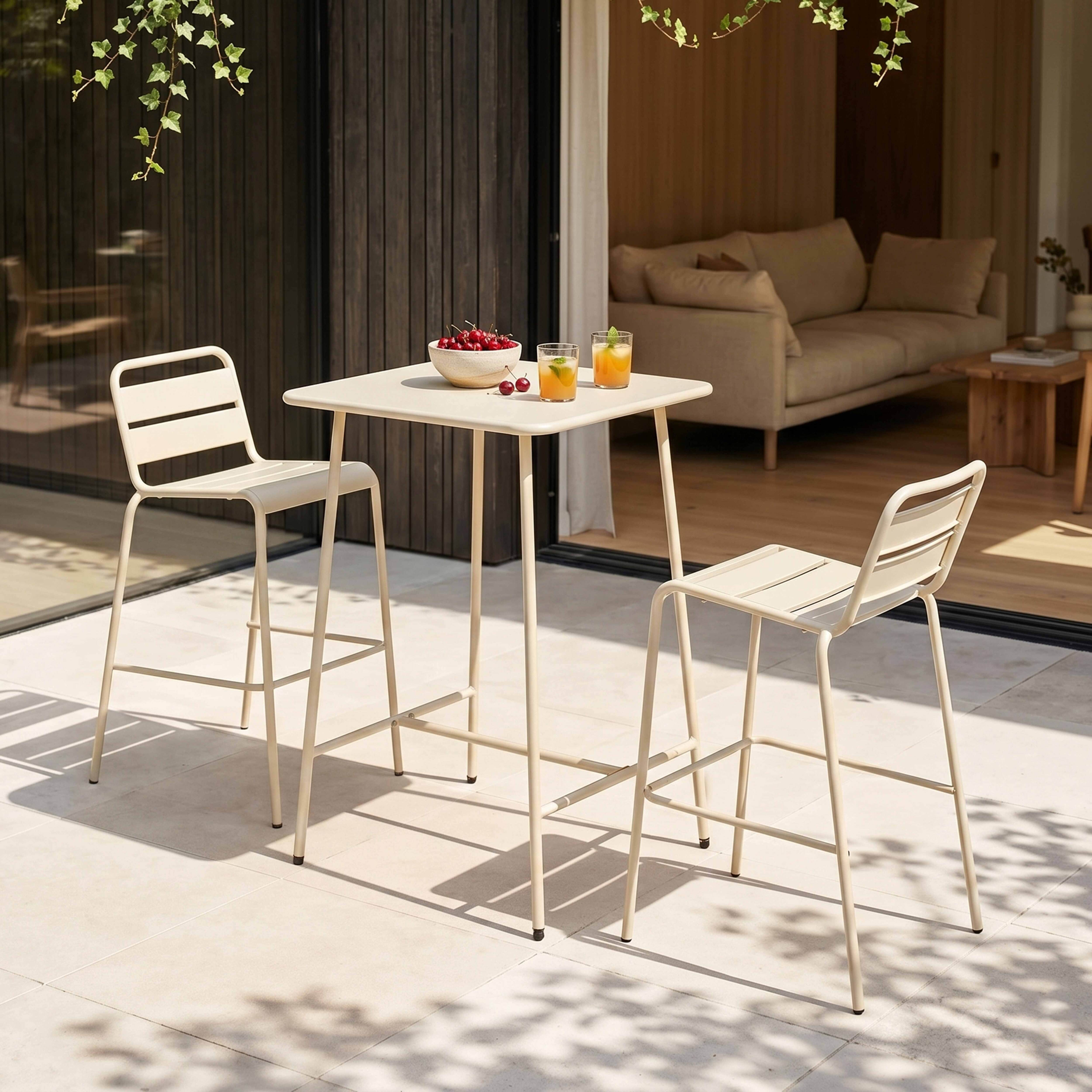 Ein beiger Bistrotisch mit zwei Hockern steht auf einer Terrasse mit Obst und Getränken.