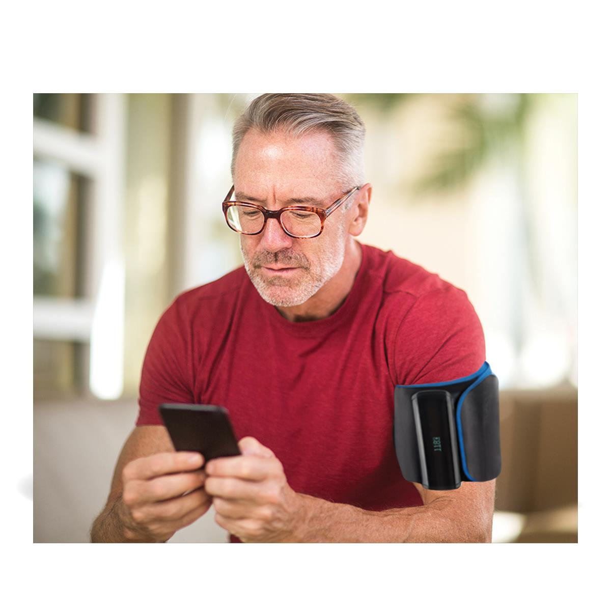 Ein Mann mit Brille und rotem Hemd benutzt ein Blutdruckmessgerät am Arm und ein Smartphone.