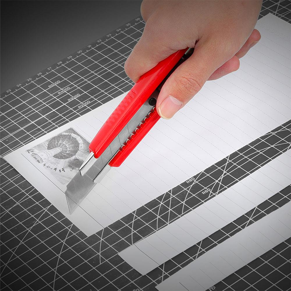 Kırmızı maket bıçağı kesme matı üzerinde resimli kağıt kesiyor.