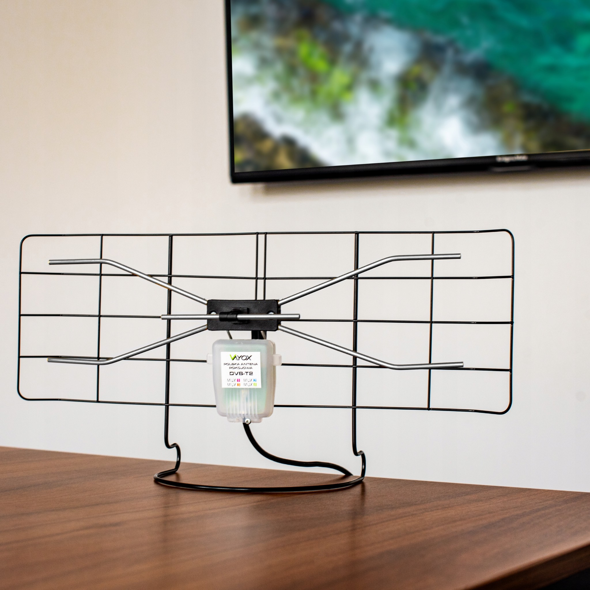 Ein schwarzer DVB-T2-Antennenständer steht auf einem Holztisch vor einem Fernseher.