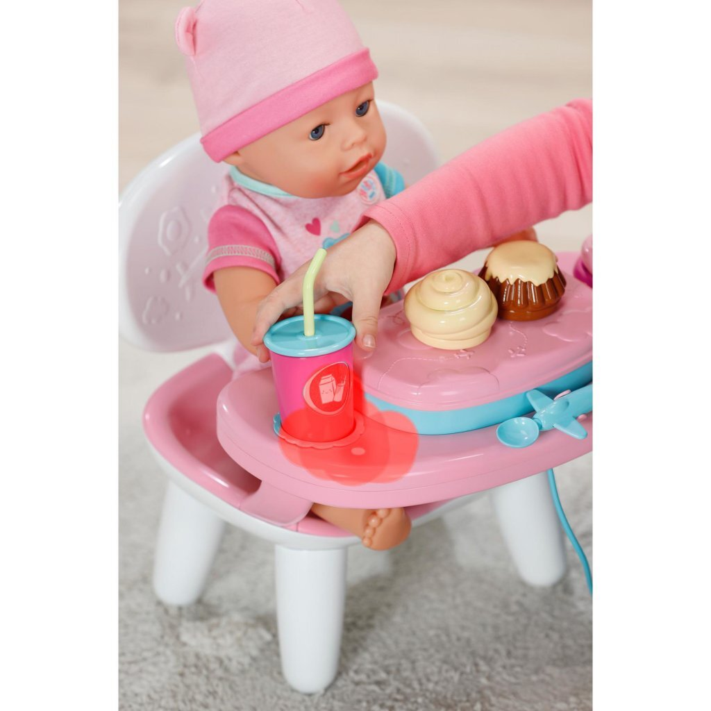 Baby-Puppe in pinker Mütze sitzt im Hochstuhl und hält pinken Becher mit Strohhalm.