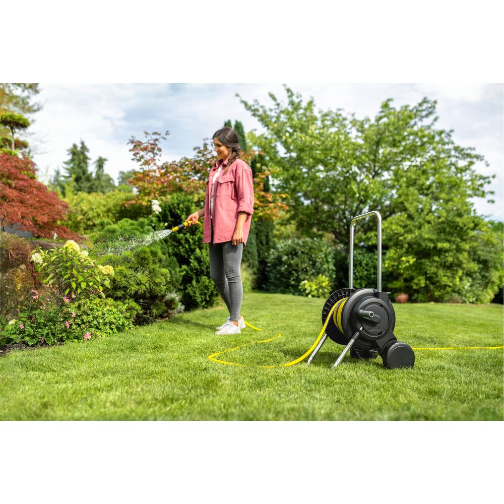 Eine Frau wässert Pflanzen mit einem Schlauch in einem üppigen Garten.