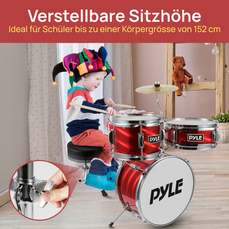 Junge mit Narrenkappe spielt auf roter Trommel. Teddybär sitzt im Hintergrund.