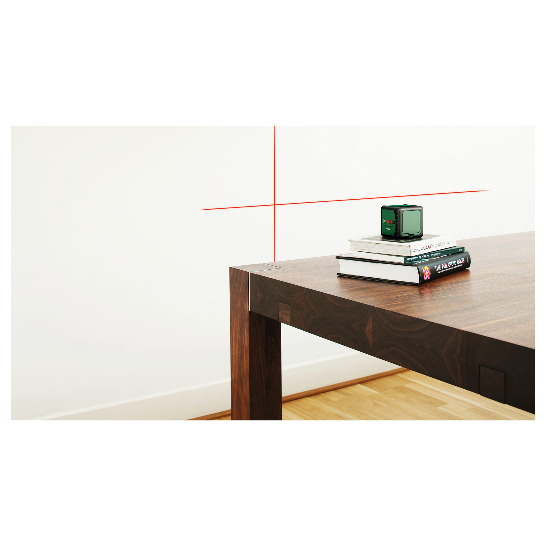 Ein grünes Bosch-Laser-Messgerät auf Büchern auf einem Holztisch. Rote Linien auf der Wand.