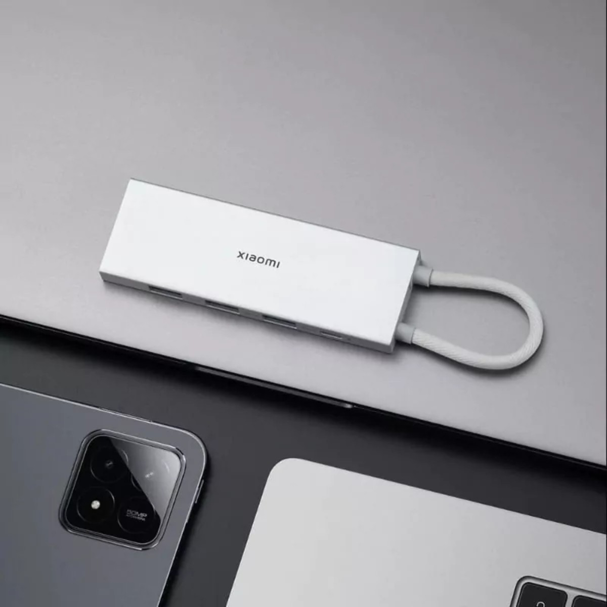 Un hub USB-C blanco de Xiaomi con cables descansa sobre un portátil junto a un smartphone gris.