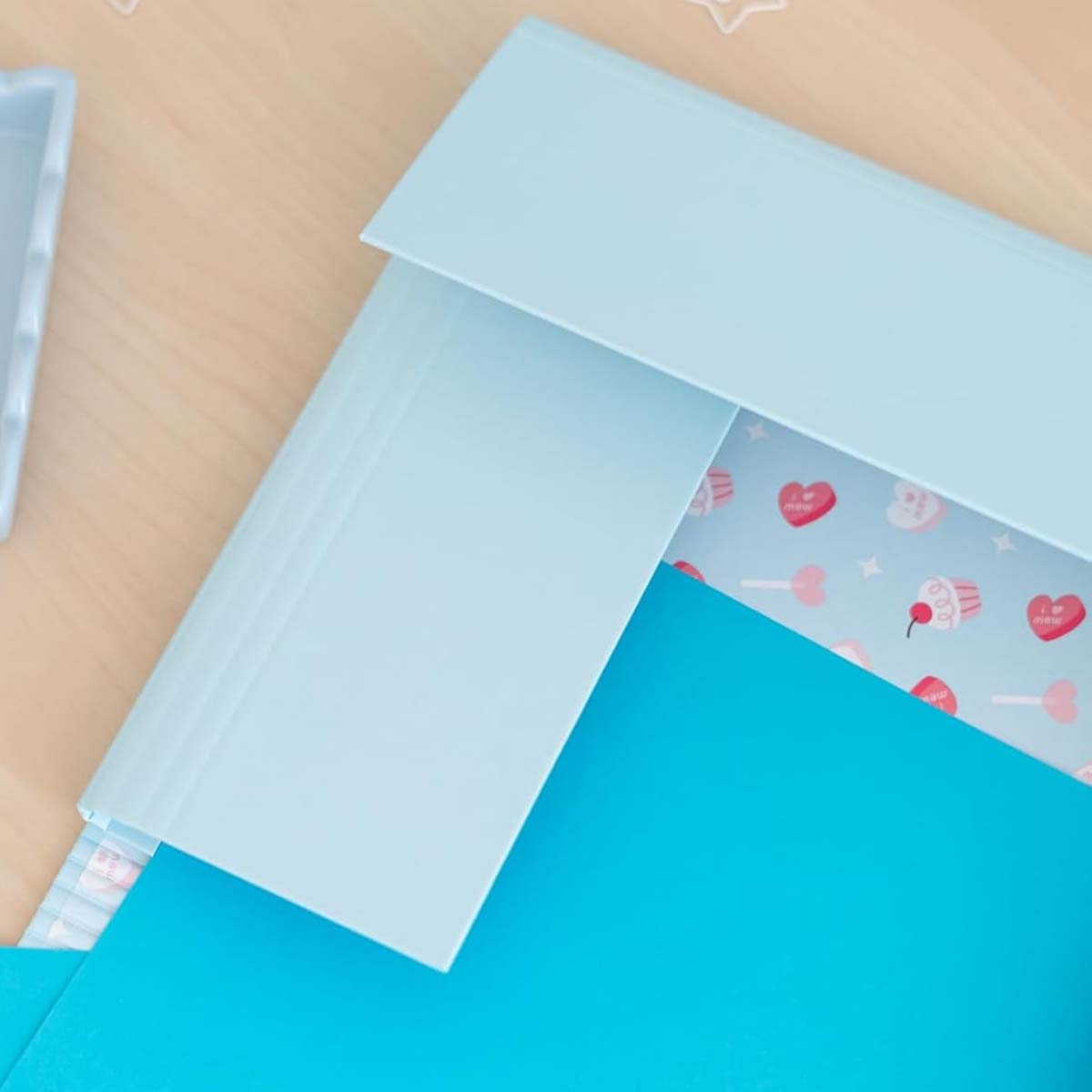 Hellblaue und blaue Ordner auf einem Holztisch mit Herz- und Cupcake-Muster.