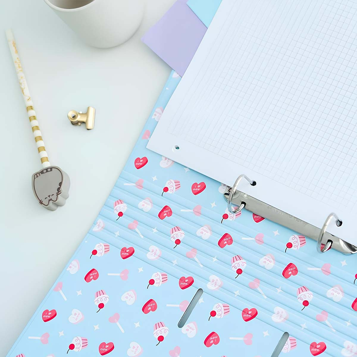 Hellblauer Ordner mit Cupcake- und Herzmuster. Notizbuch und Bleistift daneben.