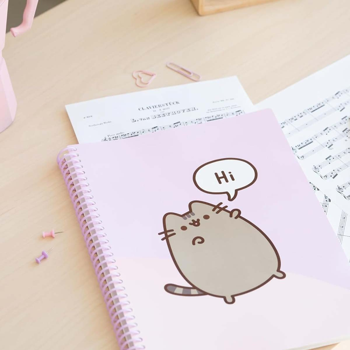 Ein Notizbuch mit Pusheen der Katze, die 'Hi' sagt, auf einem Schreibtisch mit Noten.