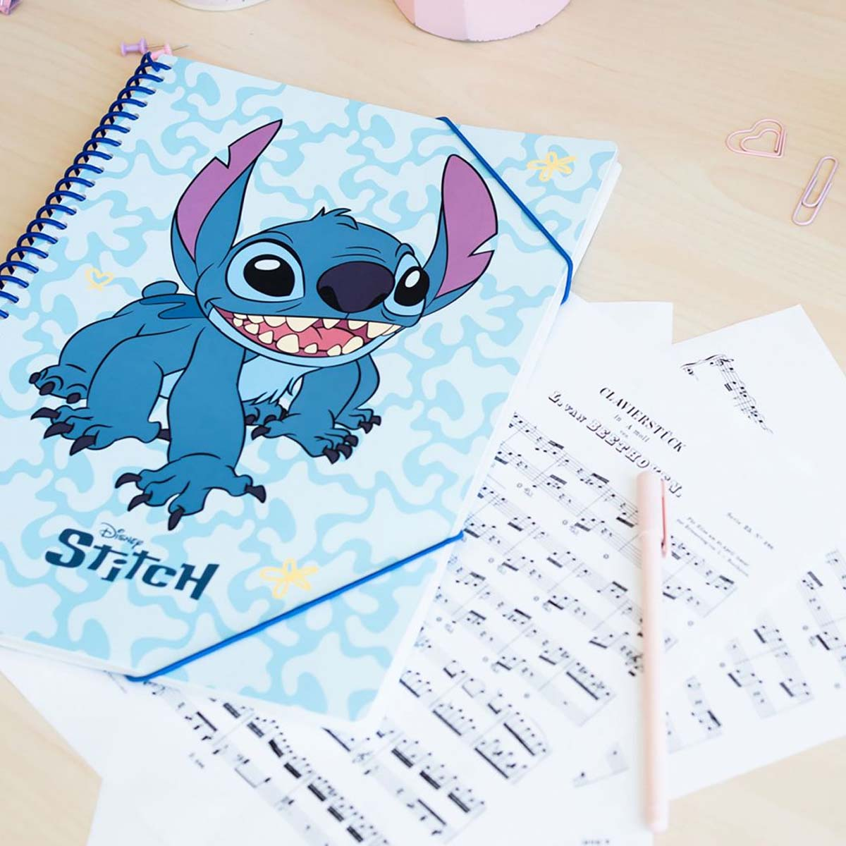 Ein blauer Notizblock mit Stitch drauf, daneben Notenblätter und Stift.